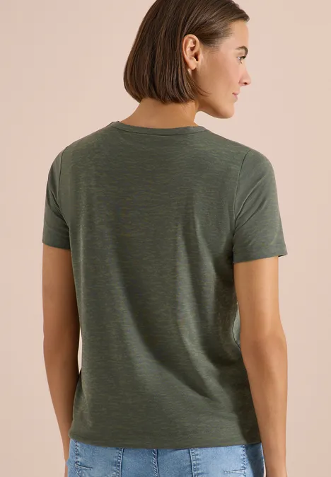 Frau von hinten mit olivgrünem T-Shirt und dunkler Hose vor hellem Hintergrund.